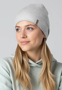 Grijze gebreide muts met een zachte textuur, een afgeronde vorm en een klein bruin stoffen label aan de zijkant; gedragen met een lichtgroene hoodie.