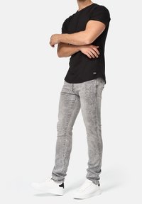 Camiseta negra de manga corta combinada con jeans skinny gris claro. El modelo lleva zapatillas blancas con detalles negros. Diseño casual y ajustado.