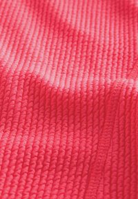Tessuto testurizzato di un brillante colore rosa, caratterizzato da righe e una finitura liscia. Il materiale appare morbido e leggermente elasticizzato.