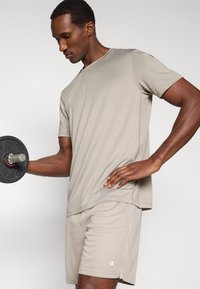 Αθλητική μπλούζα και σορτς ανοιχτό γκρι, κατασκευασμένα από διαπνέον ύφασμα. Διαθέτουν εφαρμοστή σχεδίαση με διακριτικές ραφές και λογότυπο στο στήθος.