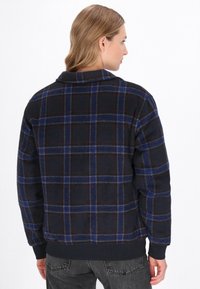 Svart och blå rutigt flanellskjorta med krage, ribbade manschetter och nederkant, med mjuk textur och avslappnad passform.