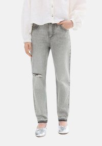 Grå slitna jeans i denim med ett rivet knä, med en avslappnad passform och uppkavlade muddledningar, tillsammans med en vit skjorta och silvriga ballerinaskor.