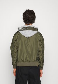 Olivgrüne Bomberjacke mit grauem Kapuzenfutter, gerippten Bündchen und Saum. Verfügt über ein Logo am Kragen und eine glatte, glänzende Textur.