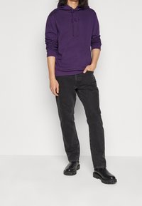 Sudadera con capucha en color púrpura y bolsillo frontal, combinada con jeans de mezclilla negros y botas de tobillo negras. Tela suave con puños acanalados.