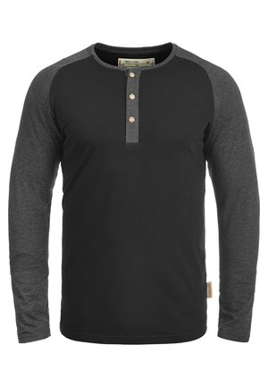 Koszula z długim rękawem o czarnym korpusie i szarych rękawach raglanowych. Posiada okrągły dekolt oraz trzy guziki na plastrze na klatce piersiowej.