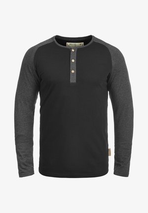 Maglietta a maniche lunghe con corpo nero e maniche raglan grigie. Presenta un collo rotondo e una patta con tre bottoni sul petto.