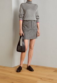 Pull en laine gris à col roulé, jupe pied-de-poule noir et blanc, mocassins en cuir noir et sac à main structuré noir. Textures lisses, coupe ajustée.