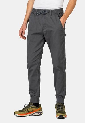 Graue Jogginghosen mit elastischem Bund und Kordelzug, ausgestattet mit Seitentaschen. Tragen Sie dazu olivgrüne Sneakers mit orangefarbigen Akzenten.
