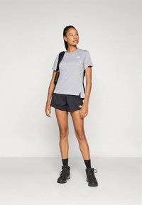 Grå t-skjorte med korte ermer og logo, kombinert med svarte shorts. Svarte tursko og en ryggsekk fullfører det athletiske antrekket.