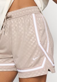 Bēge sporta šorti ar teksturētu šaha rakstu, baltām sānu strīpām, elastīgu jostasvietu un mazu Nike logo priekšpusē.