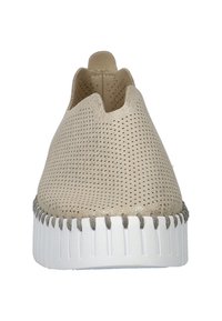 Zapatos beige de tela perforada tipo slip-on con puntera redondeada, parte superior texturizada, lados elásticos y una gruesa suela de goma blanca con detalles de costura.