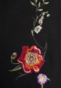 Tissu noir avec une broderie florale complexe en rouge, orange et violet, avec des feuilles vertes et des détails fins sur une surface lisse.
