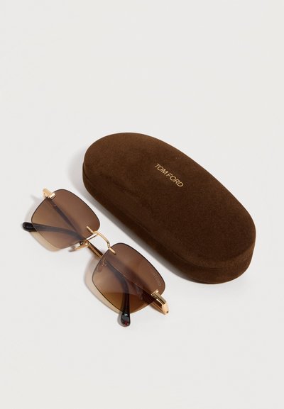 Brown-tinted rectangular sunglasses with gold frames next to a matching brown Tom Ford branded hard case on a white surface.