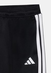 Zwarte sportbroek met een gladde textuur, voorzien van witte zijstrepen en een klein wit logo op de onderkant van het linkerpootje. Inclusief elastische tailleband.