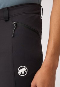 Zwarte outdoorbroeken met een ritszak, voorzien van een gestructureerde afwerking en een wit logo van een olifant in een cirkelontwerp.
