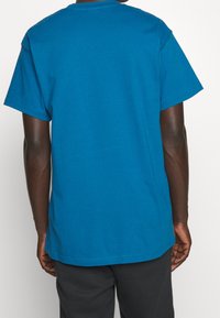 Modré bavlněné tričko s krátkým rukávem, kulatým výstřihem a jednoduchým designem. Má volný střih a minimální šití na lemu.