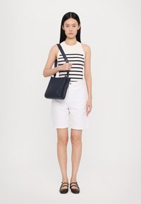 Sac en cuir bleu marine à bandoulière réglable, texture lisse, forme rectangulaire. Modèle portant un débardeur rayé et un short blanc.