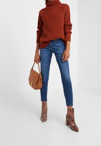 Rust ribbed turtleneck sweater, blue jeans, brown handbag, and ankle boots in a textured snake print with a block heel.