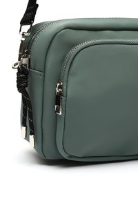 Borsa in nylon verde con texture, due compartimenti con zip, dettagli in hardware argento e una tracolla bianca e nera. Forma compatta e rettangolare.