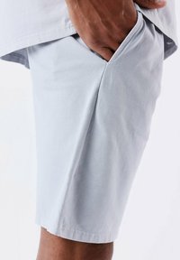 Pantalones cortos gris claro hechos de una tela suave, con bolsillos laterales y un corte relajado, con un dobladillo limpio y costuras mínimas.