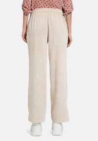 Kermanharmaatbeige, joissa on leveät lahkeet ja elastinen vyötärö, jossa on pystysuora röyhelötekstuuri. Yhdistetty valkoisiin lenkkareihin.