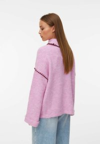 Pull en tricot rose avec une coupe décontractée, doté d'un col haut, de finitions contrastantes marron le long de l'encolure et des manches, et d'une texture douce.