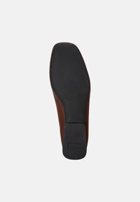 Suela de zapato de cuero marrón con una parte inferior de goma negra. La suela es lisa con un patrón texturizado cerca del dedo del pie y un tacón cuadrado.