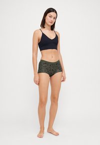 Čierny bralet s tenkými ramienkami a dizajnom do V, skombinovaný s olivovozelenými nohavičkami typu boyshorts so vzorom listov. Mäkko a elastické látky.
