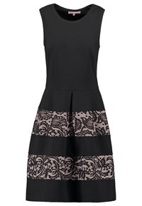 Robe noire sans manches avec un corsage ajusté, une jupe évasée, et deux panneaux horizontaux en dentelle beige ornés de motifs floraux.