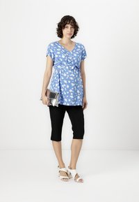 Top azzurro chiaro con motivo floreale bianco, scollatura a V, maniche corte e cintura in vita. Pantaloni neri cropped e pochette argentata. Sandali bianchi con tacco.