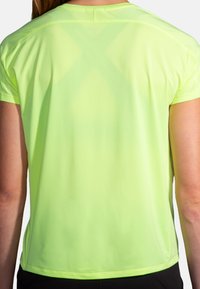 T-shirt de sport fluorescent jaune à manches courtes, en tissu léger avec texture évacuant l'humidité. Présente une coupe décontractée et un détail de couture à l'arrière.