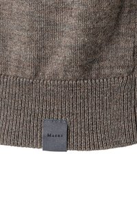 Närbild av brun stickad tyg med ribbat mönster och en liten svart etikett sydd vid nederkanten.