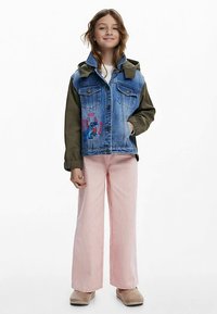 Džinsinė striukė su alyvuogių žaliomis rankovėmis, puošta mėlyno personažo pieštiniu, derinama su šviesiai rožinėmis plačiomis kelnėmis.