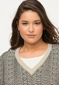 Suéter de pico con un patrón de zigzag texturizado en negro y crema, que presenta un tejido ligero y un ribete en beige contrastante en el escote.