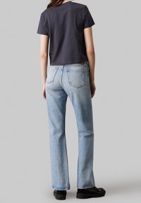 Camiseta corta de color gris oscuro, jeans rectos de color azul claro, botas gruesas negras. Presenta costuras distintivas y bolsillos traseros en los jeans.