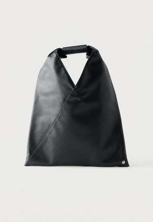 Geantă tote triunghiulară neagră din piele, cu mâner pliat înfășurat în piele asortată, pe un fundal simplu, deschis la culoare.