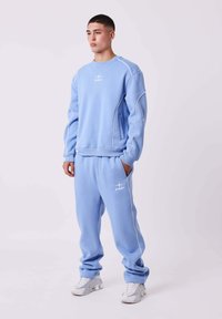 Lichtblauwe sweatshirt- en broekset met witte stiksels en logo. Gemaakt van zachte stof, met een ontspannen pasvorm en zijzakken.