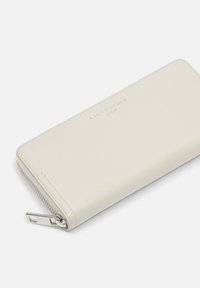 Portefeuille en cuir beige clair avec une texture lisse, doté d'une fermeture éclair argentée et du nom de la marque en relief, au design rectangulaire élégant.