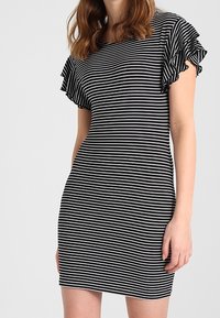 Robe à rayures noires et blanches avec des manches courtes à volants, une coupe ajustée, un tissu doux et un col rond.