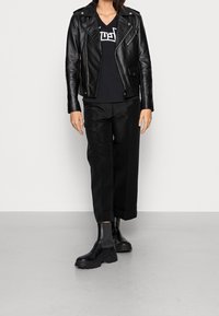 Czarna skórzana kurtka motocyklowa z zamkami, czarny T-shirt V-neck, dopasowane czarne spodnie oraz masywne czarne botki za kostkę, na neutralnym tle.