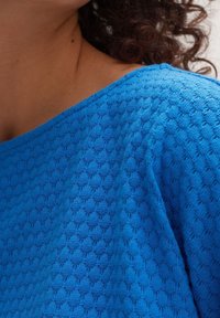 Niebieski dzianinowy top z fakturowanym wzorem, okrągłym dekoltem i krótkimi rękawami, wykonany z lekkiego i przewiewnego materiału.