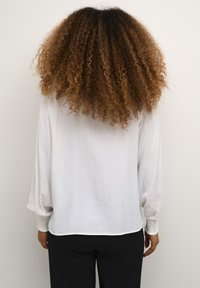 White, lightweight blouse with long, puffed sleeves and gathered cuffs. Soft texture with a relaxed fit, paired with black trousers.