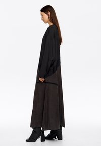 Długa czarna sukienka z koronkowymi akcentami i luźnym krojem, z warstwowym designem i kontrastującymi fakturami. Noszona z botkami na obcasie sięgającymi kostki.