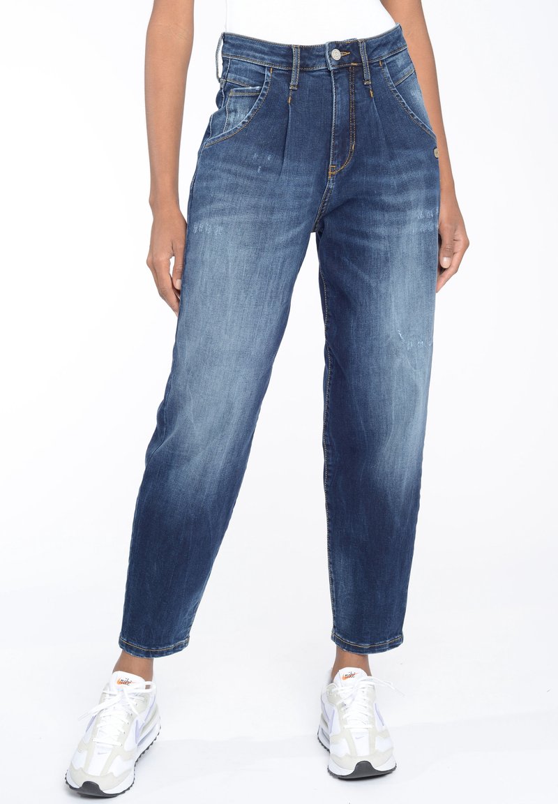 Denimjeans i en medel tvätt med hög midja och avsmalnande ben. Har två framfickor och subtila blekningar. Bärs med vita sneakers.