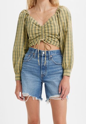 Femme portant un crop top froncé à carreaux jaunes avec des manches bouffantes et un short en jean effiloché taille haute.