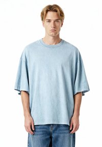 Ljusblå oversized t-shirt i bomull med rund hals, nedhasade axlar och korta ärmar. Slät yta med subtila färgvariationer.