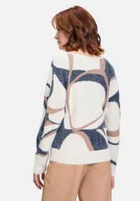 Flauschiger Cremepullover mit abstrakten Mustern in Blau, Beige und Schwarz. Hat eine lockere Passform und lange Ärmel sowie einen weiten Ausschnitt.