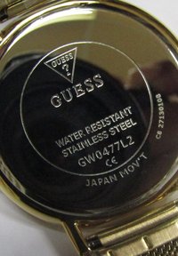 Arany színű rozsdamentes acél óra hátlap, gravírozott "GUESS." logóval. Jellemzők közé tartozik a vízállóság, a "GW0477L2" modell szám, és a "JAPAN MOV'T." felirat.