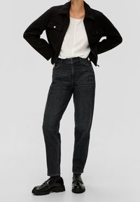 Giacca nera corta, t-shirt bianca, jeans scuri a vita alta e mocassini neri lucidi. Design semplice con tasche e cerniere visibili.