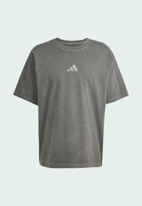 Pilkas laisvas kirpimo T-shirt su trumpomis rankovėmis, puikiai išryškinantis subtilų atspindintį trijų juostų logotipą ant krūtinės. Pagamintas iš minkštos, tekstūruotos medžiagos.